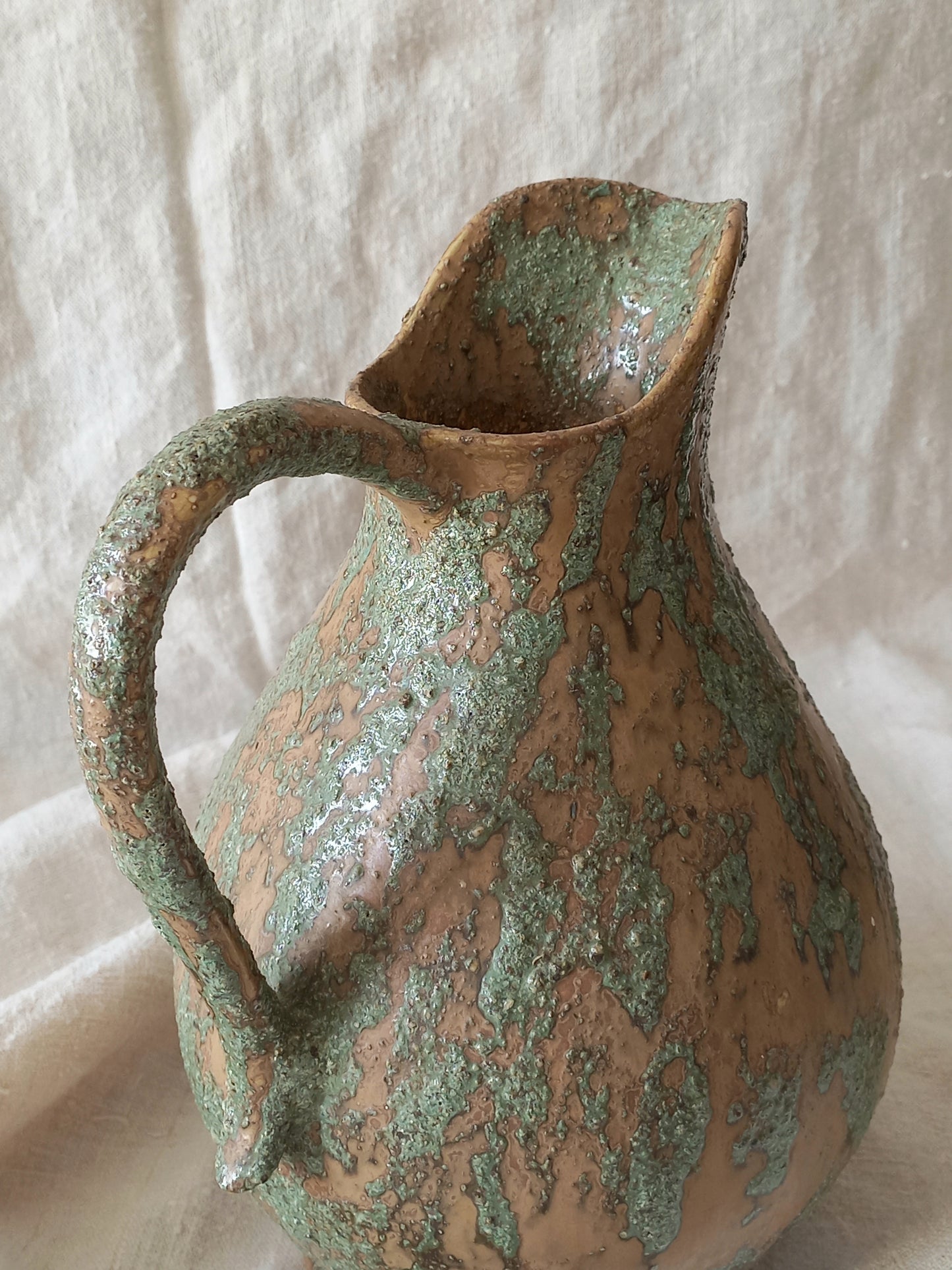Large artisan made vintage pottery jug with green and earth tones on a beige background