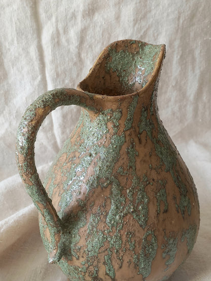 Large artisan made vintage pottery jug with green and earth tones on a beige background