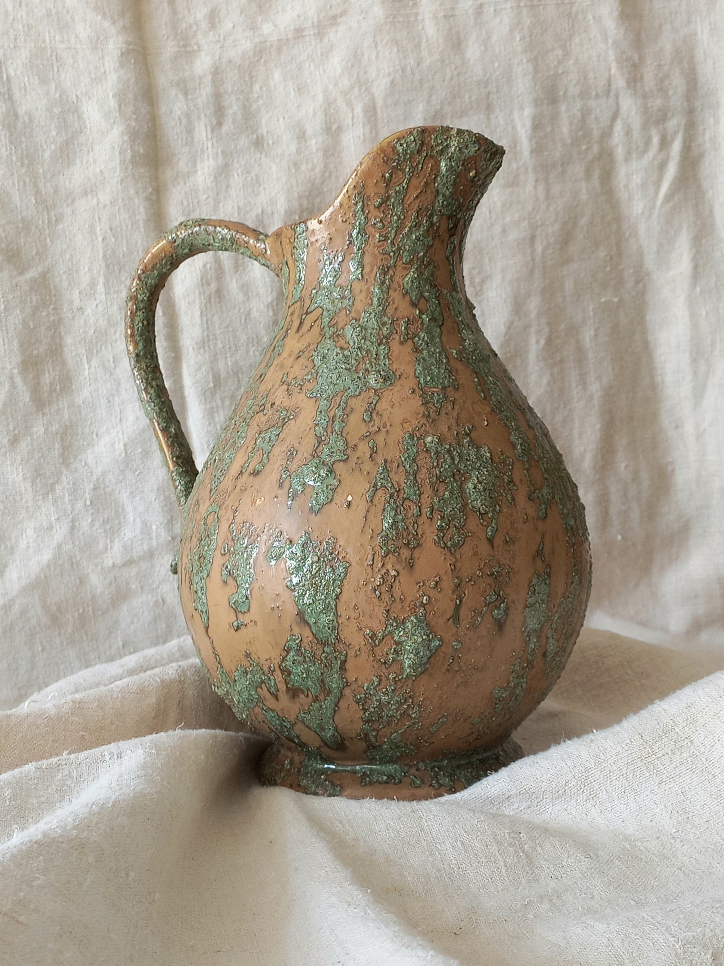 Vintage ceramic pitcher with green pattern on a textured white background