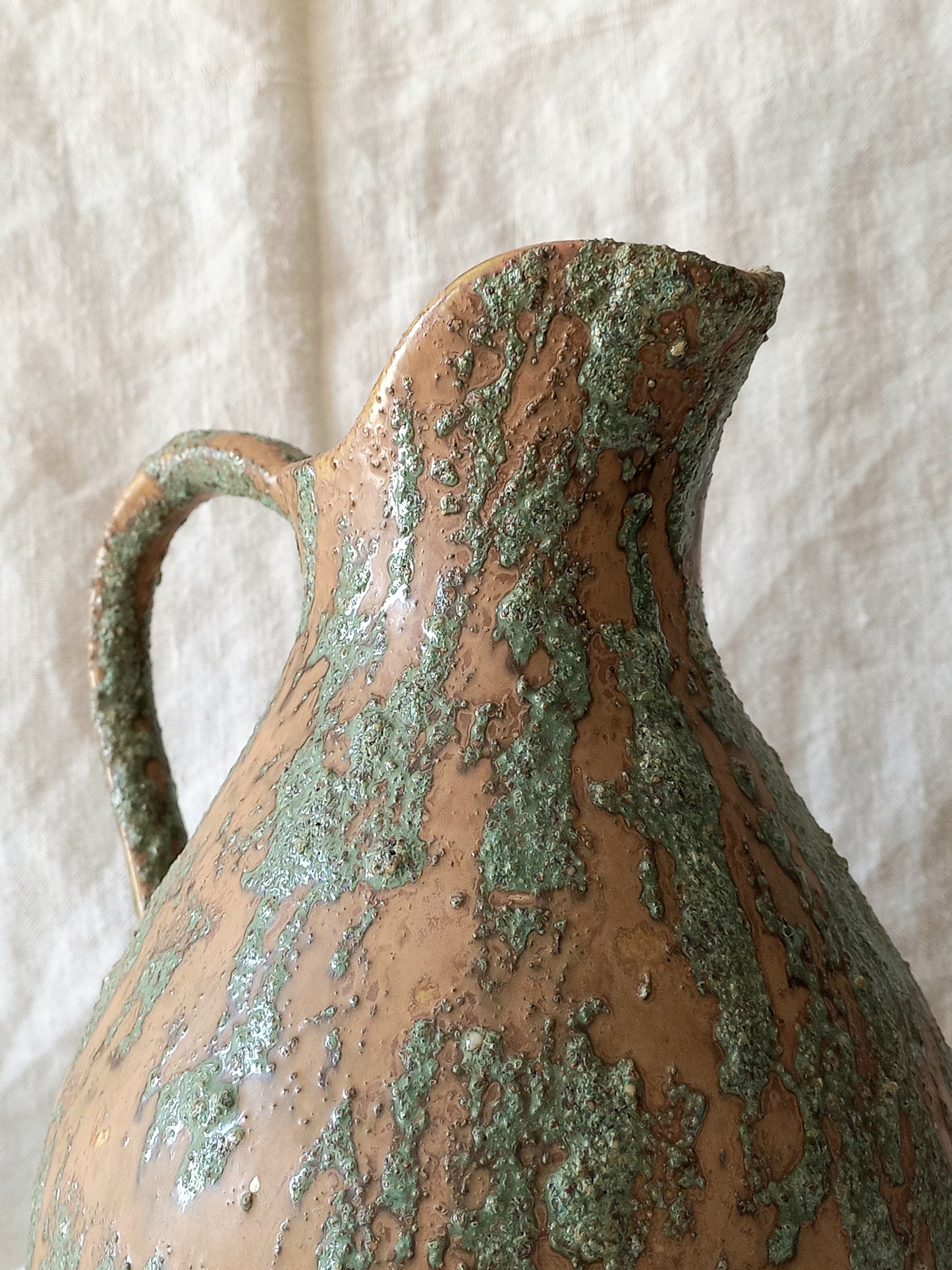 Large artisan made vintage pottery jug with green and earth tones on a beige background