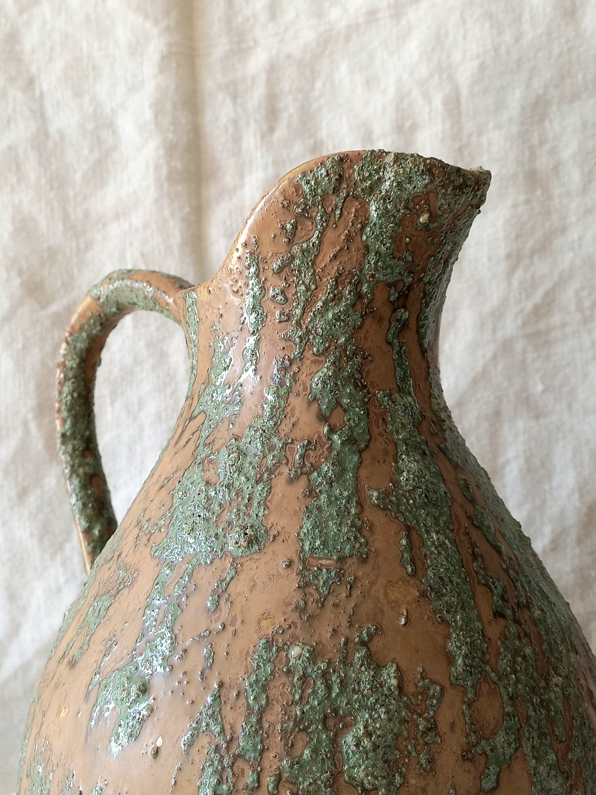 Large artisan made vintage pottery jug with green and earth tones on a beige background