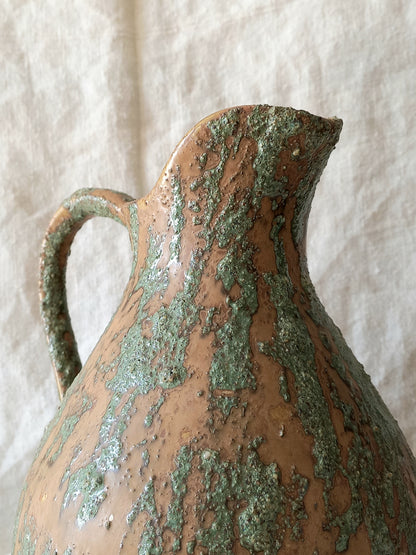 Large artisan made vintage pottery jug with green and earth tones on a beige background