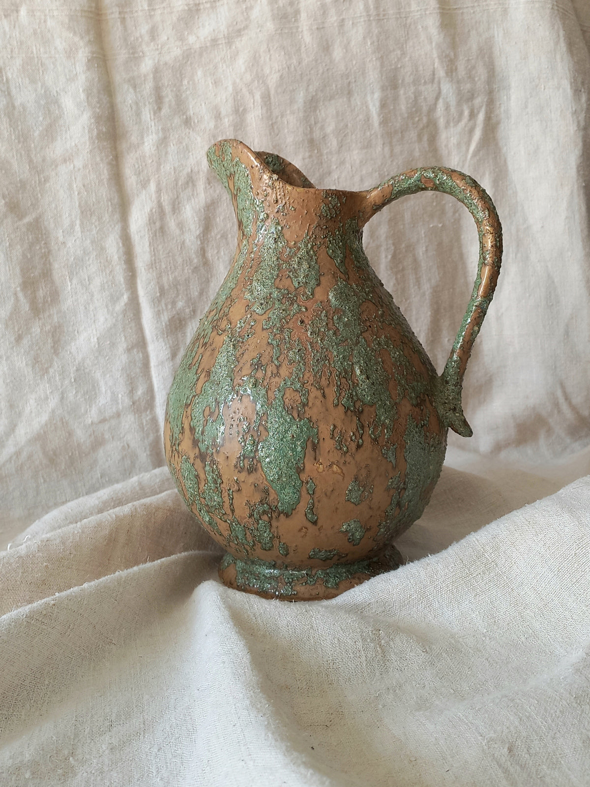 Large artisan made vintage pottery jug with green and earth tones on a beige background