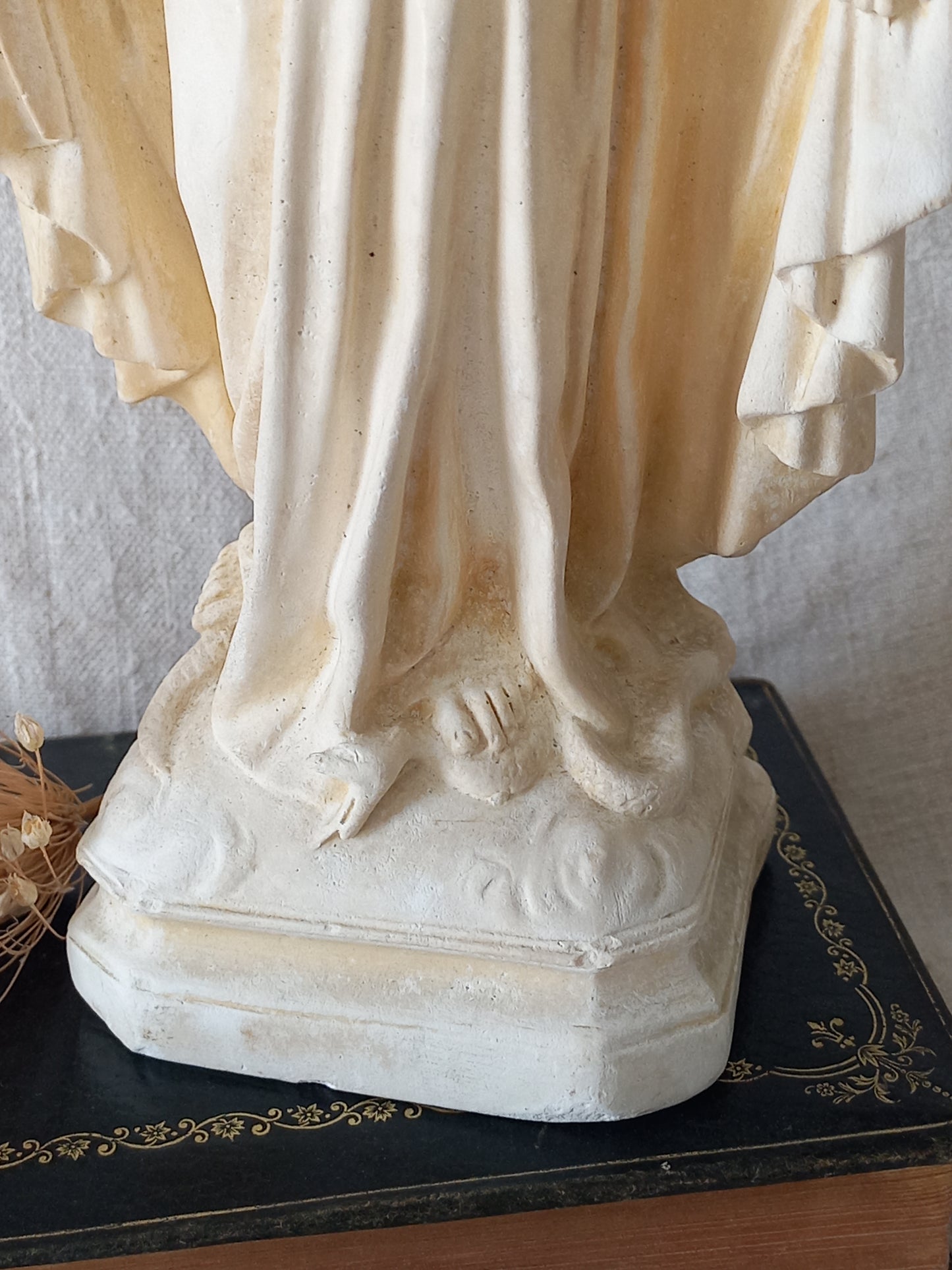 Close-up of a classical statue with detailed drapery and head on a black stand.