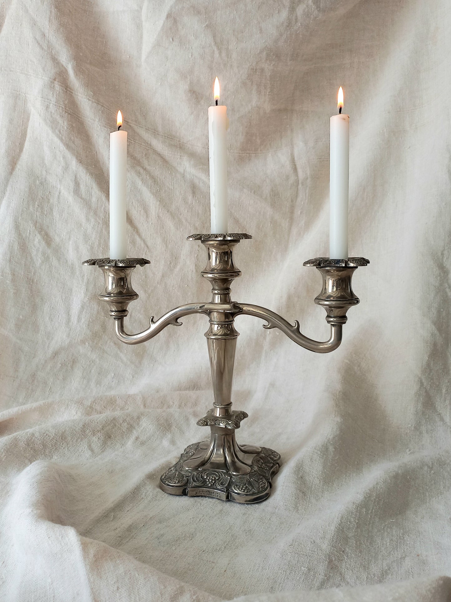Silver candelabra with three lit candles on a textured white background