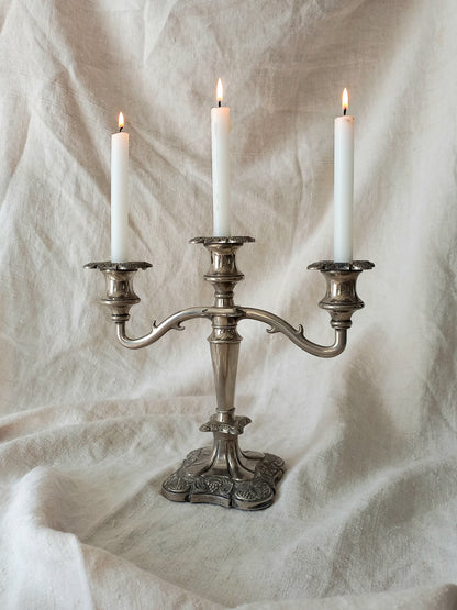 Silver candelabra with three lit candles on a textured white background