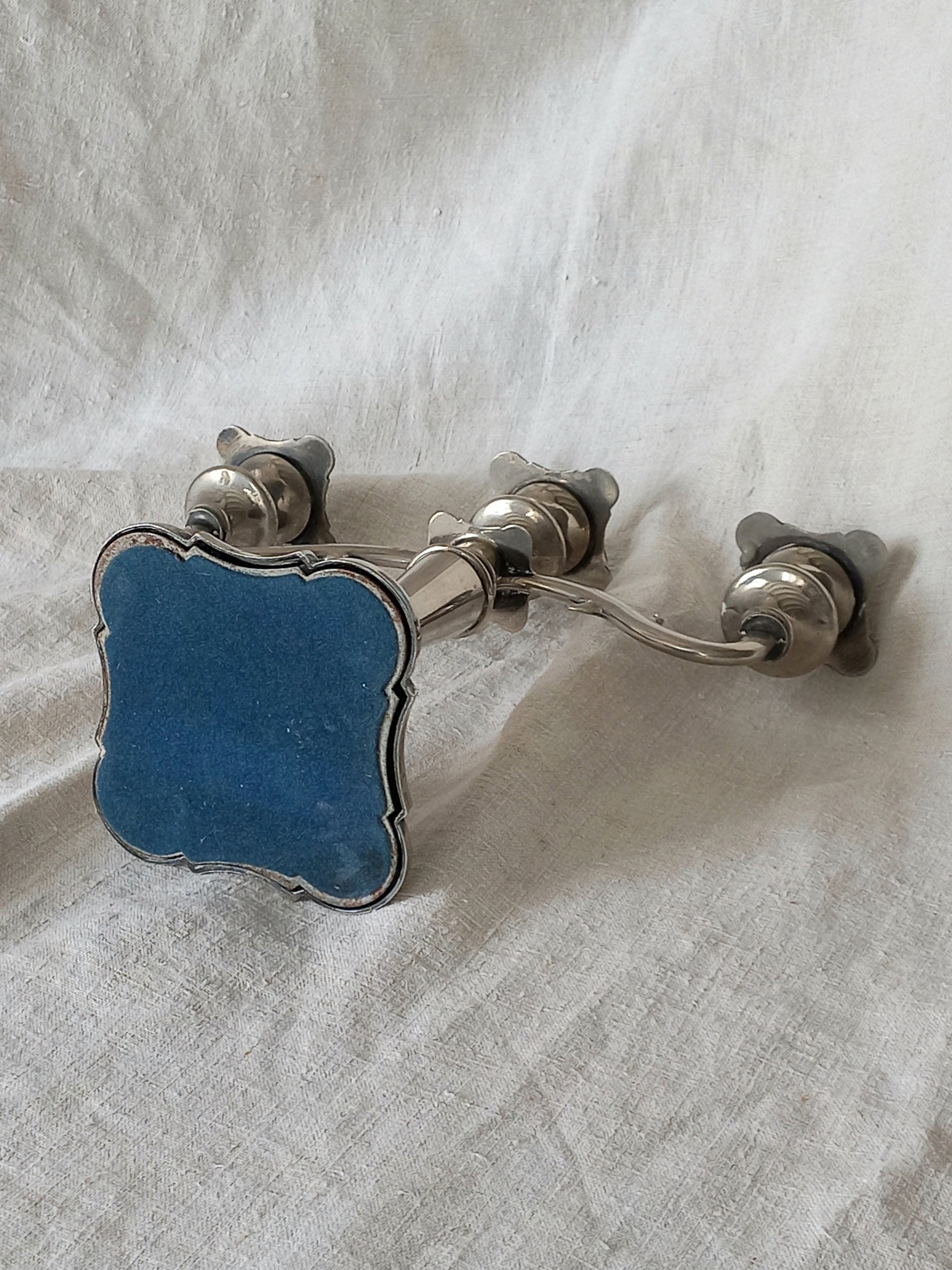 Silver candle holder with blue velvet base on a white fabric background