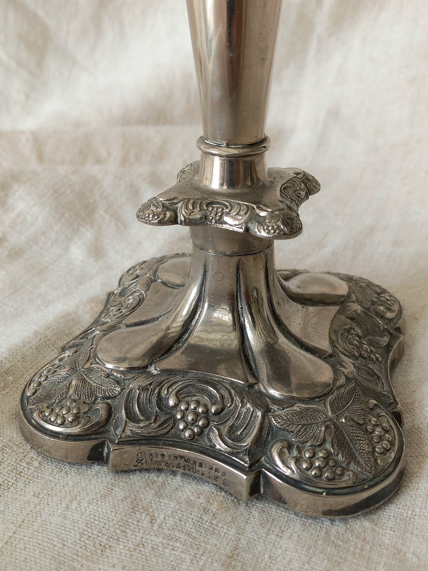 Silver candlestick with detailed design on a beige fabric background