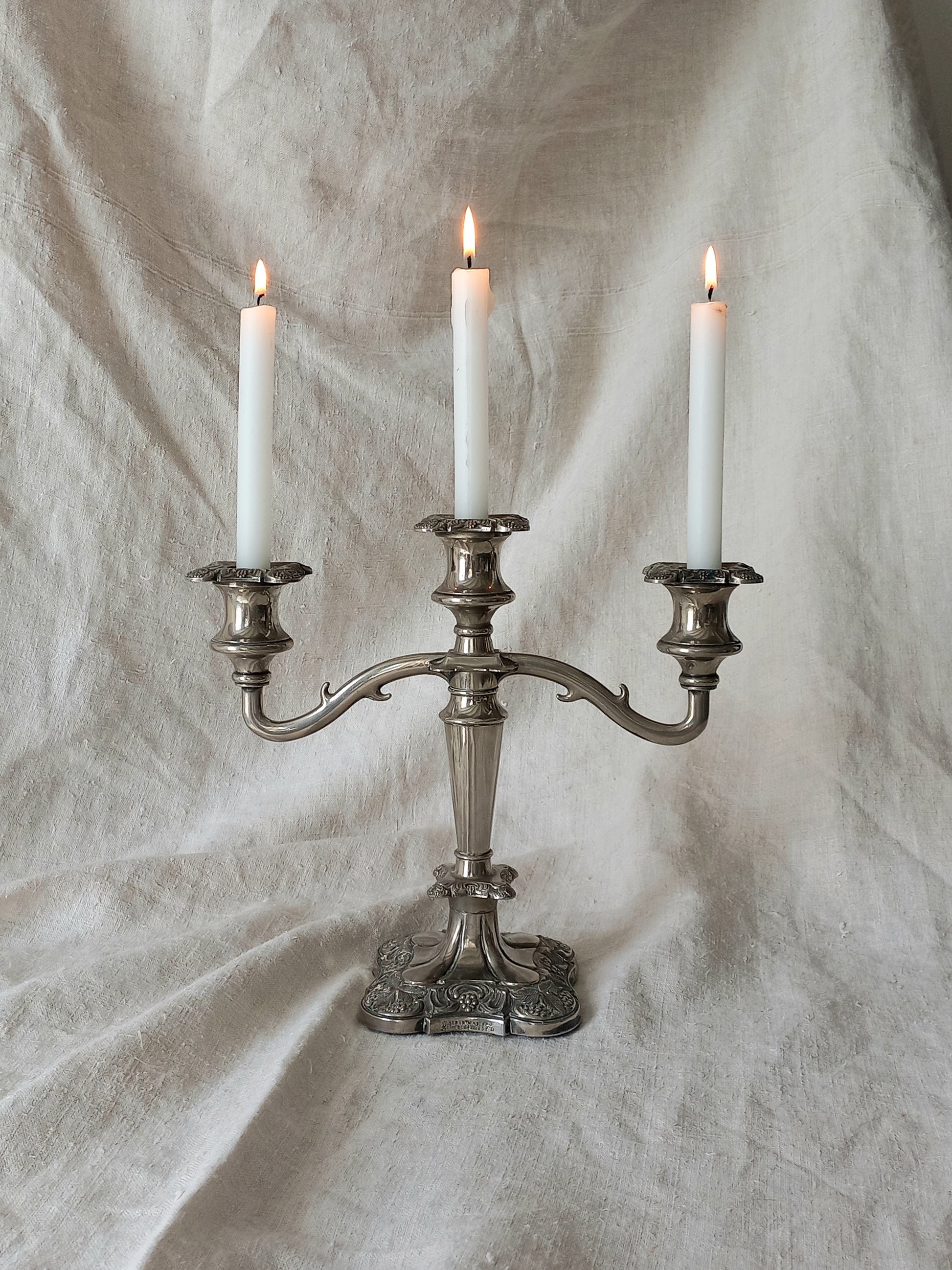 Silver candelabra with three lit candles on a textured white background