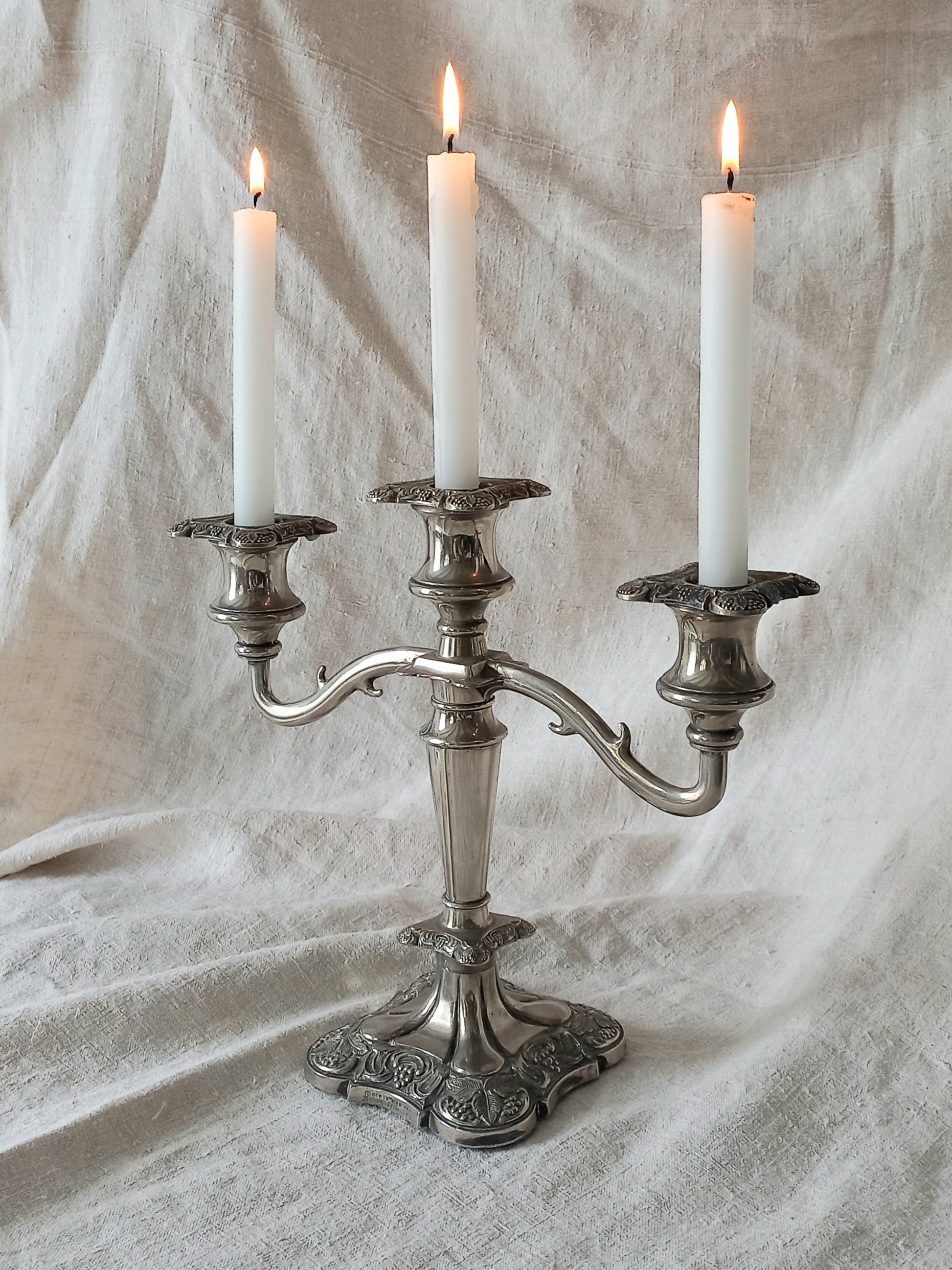 Silver candelabra with three lit candles on a textured white fabric background