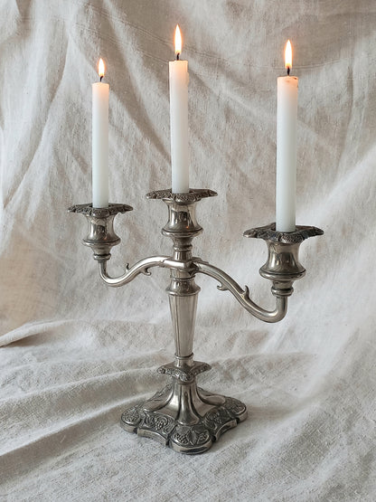Silver candelabra with three lit candles on a textured white fabric background
