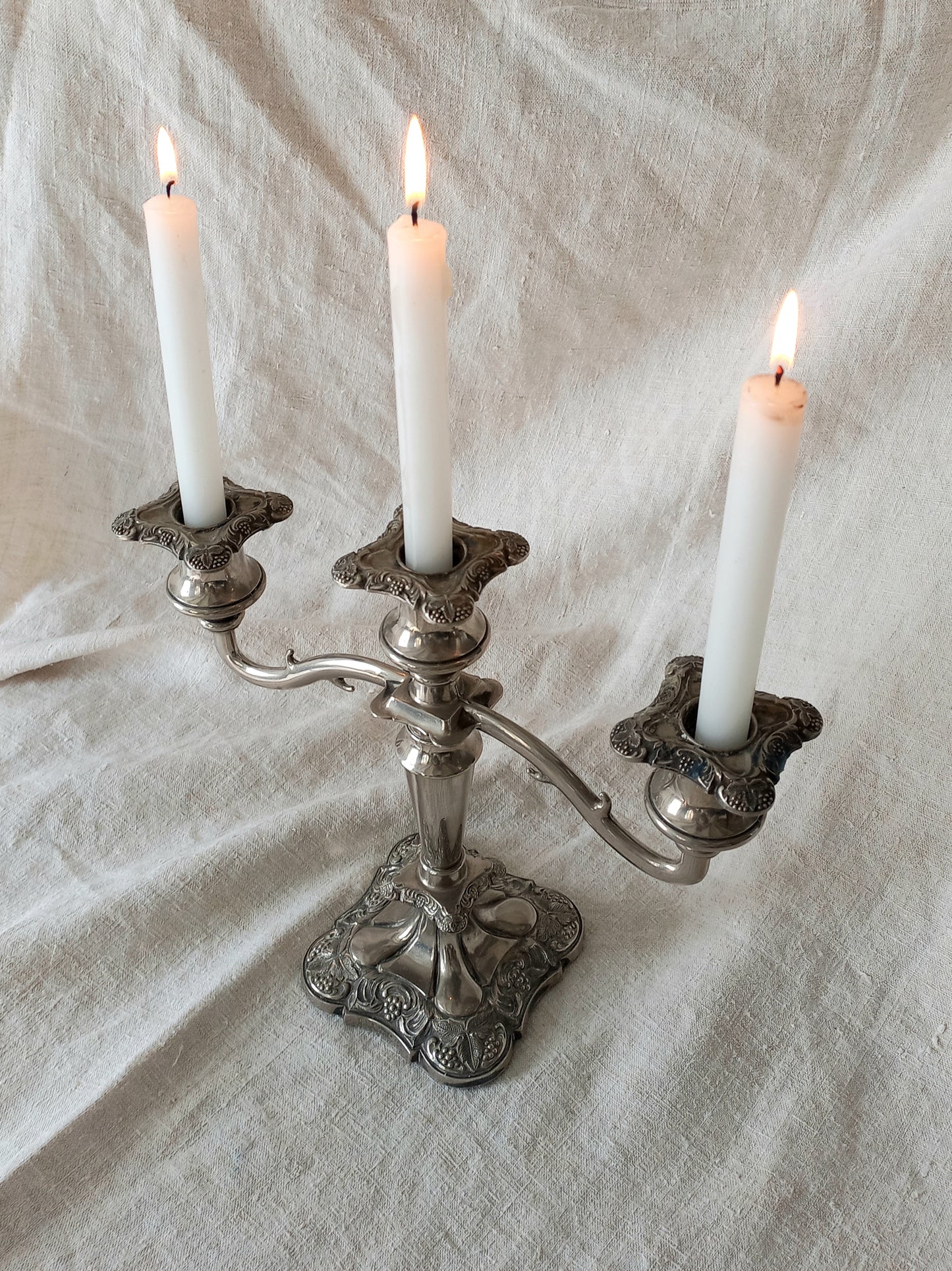 Silver candelabra with three lit candles on a textured white fabric background