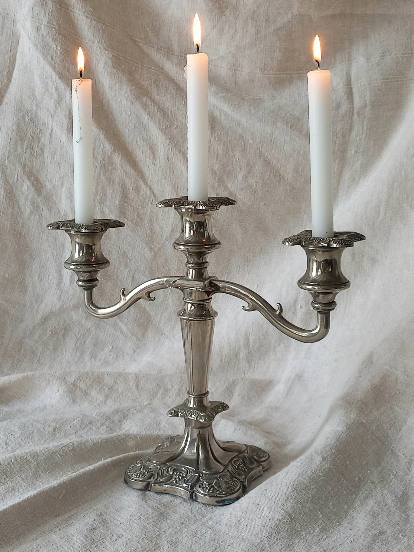 Silver candelabra with three lit candles on a textured white background