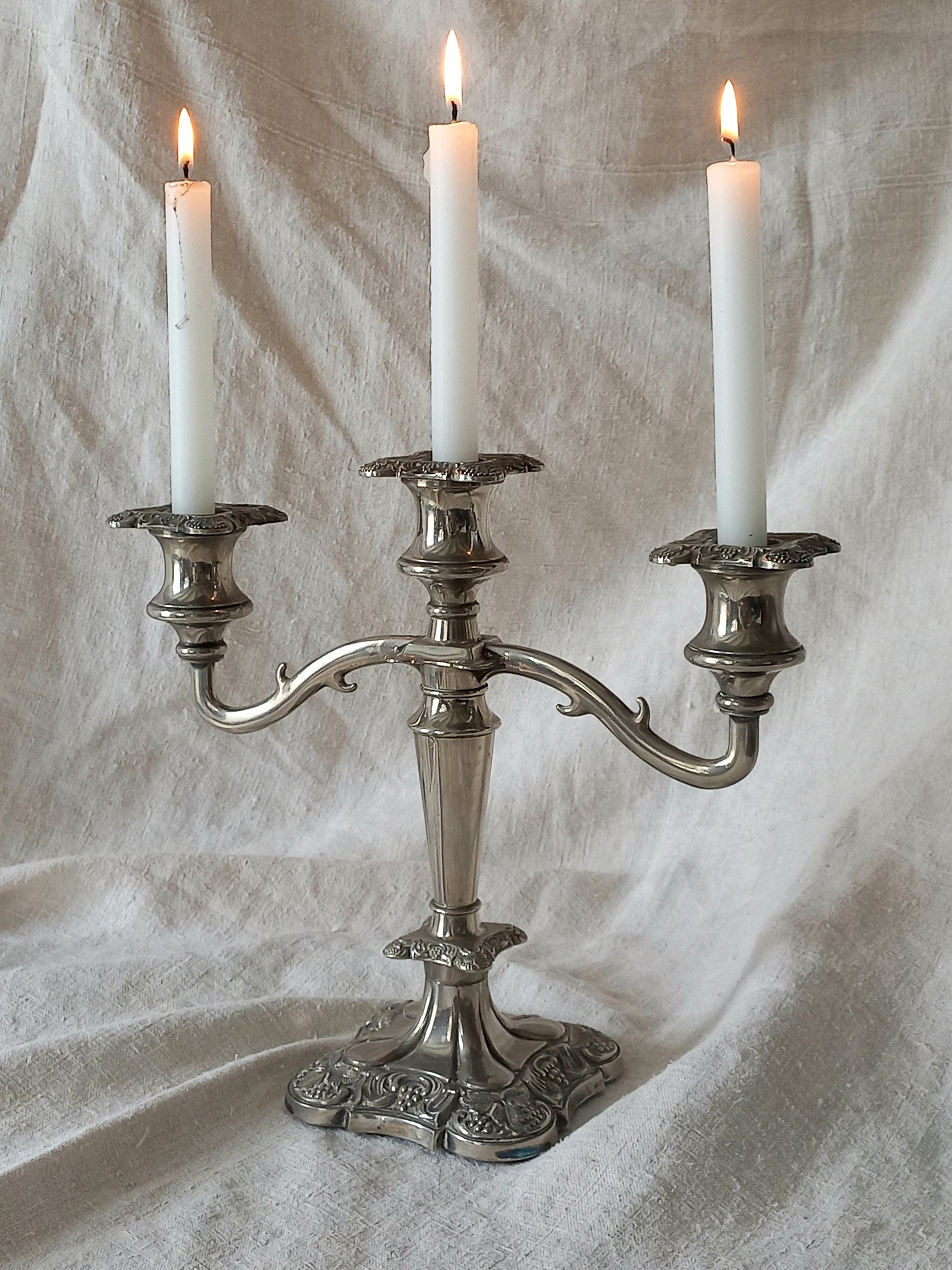 Silver candelabra with three lit candles on a textured white background
